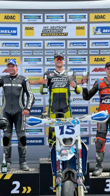 Benjamin Hagmaier auf dem Podium mit dem Pokal für den ersten Platz. Im Vordergrund seine aktuelle blaue Supermoto