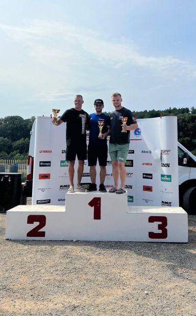 Benjamin Hagmaier mit 2 Konkurrenten auf einem weißen Podium. Er hält den Pokal für den zweiten Platz